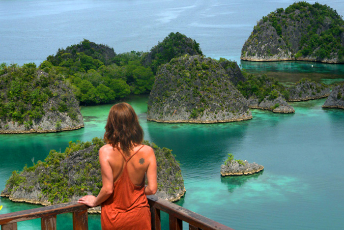 Una chica en un mirador observa los islotes repletos de vegetación que salpican un mar color verde turquesa. RAJA AMPAT. PAPÚA. INDONESIA