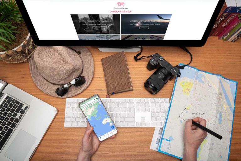 Escritorio donde se ve un mapa, gafas de sol, sombrero, una cámara, muchas de las cosas imprescindibles para hacer un viaje. Las 10 mejores webs para organizar un viaje. Descuentos para viajeros