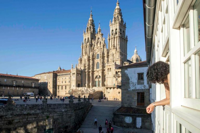 Hotel con vistas a la catedral de Santiago de Compostela. Se ve una chica asomada a la ventana disfrutando de las magníficas vistas. Descubre los 10 mejores hoteles con encanto en Santiago de Compostela. Perder el Rumbo
