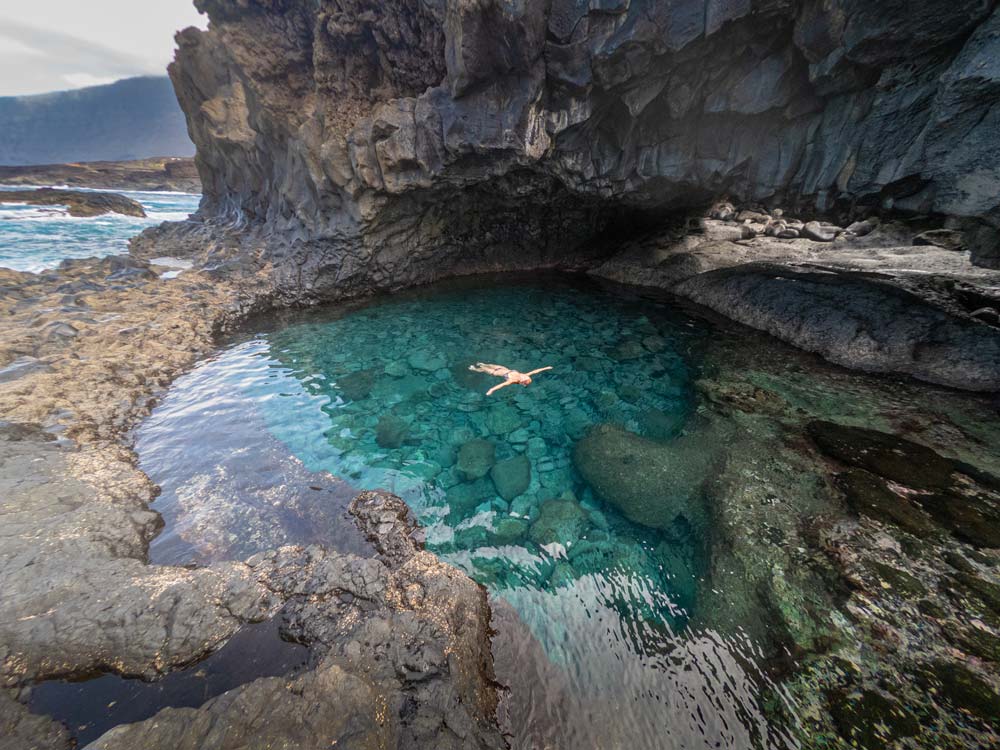 Una persona toma un baño relajante en un pozo de agua marina de color turquesa. Una de las mejores piscinas naturales de El Hierro.