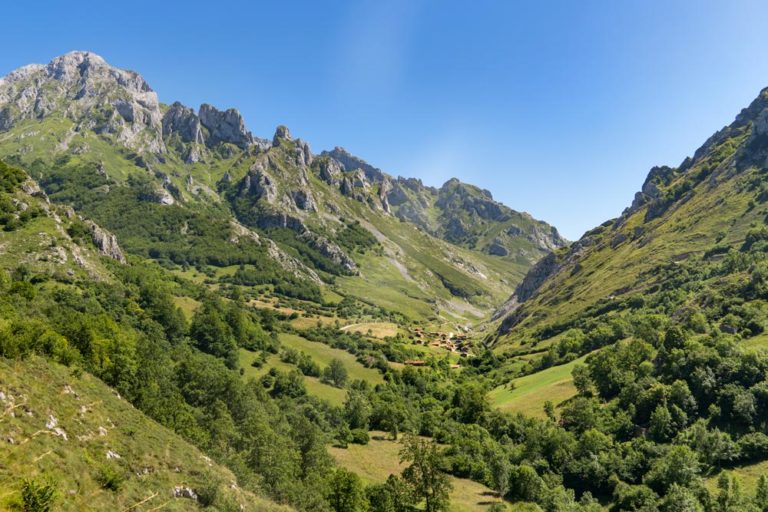 Paisaje de montañas de verdes pastos y vegetación y un pueblo en el valle. Qué ver en Asturias. 25 lugares increíbles. Perder el Rumbo