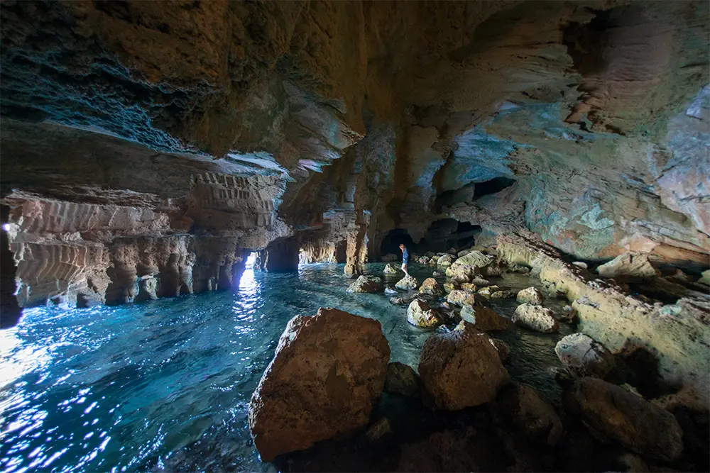 Una cueva conde se introduce el mar. Una persona debajo de una gran bóveda de piedra observa como entra el mar en la cueva.