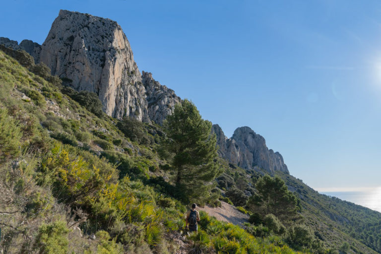 Chico que hace una ruta entre verde vegetación y elevadas montañas rocosas. Rutas de senderismo en Alicante. Perder el Rumbo