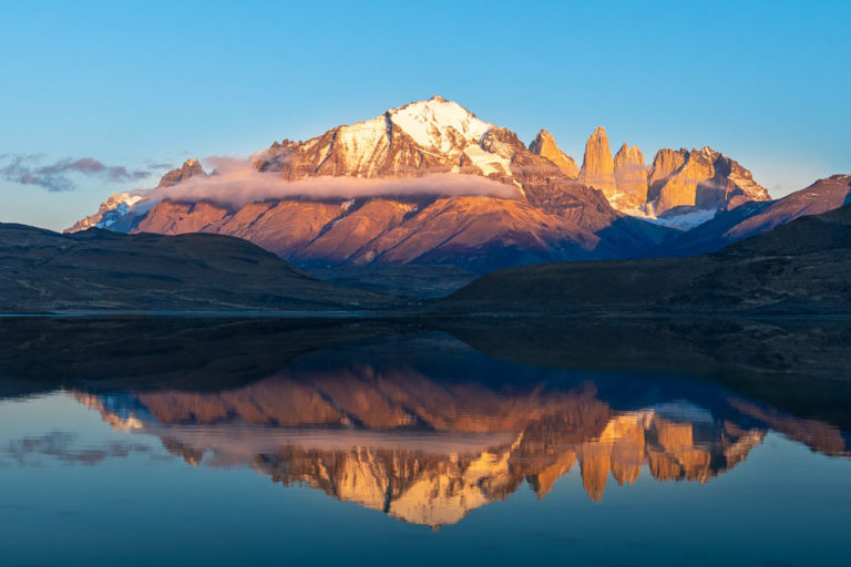 El macizo del Paine con sus torres se refleja en un lago a modo de espejo. La luz de la mañana está iluminando las partes altas de las torres. parque nacional Torres del Paine.