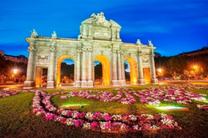 Puerta del sol iluminada en la noche. En primer término un jardín también iluminado. Maravillosa imagen de vista a los 8 mejores Free Tours en Madrid. Visitas guiadas gratuitas