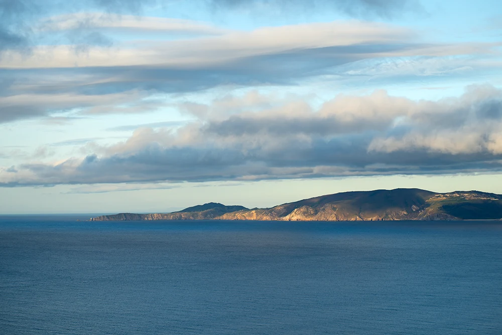 Vista lejana de la punta Estaca de Bares. El cielo medio nublado y el mar muy tranquilo.