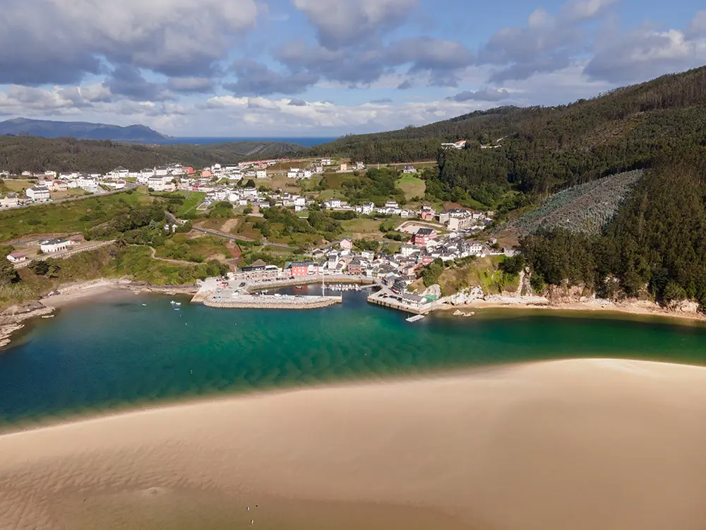 Vista aérea del pequeño pueblo de O Barqueiro con su pequeño puerto y las casas rodeando a este. En primer termino una lengua de arena del estuario del río Sor.