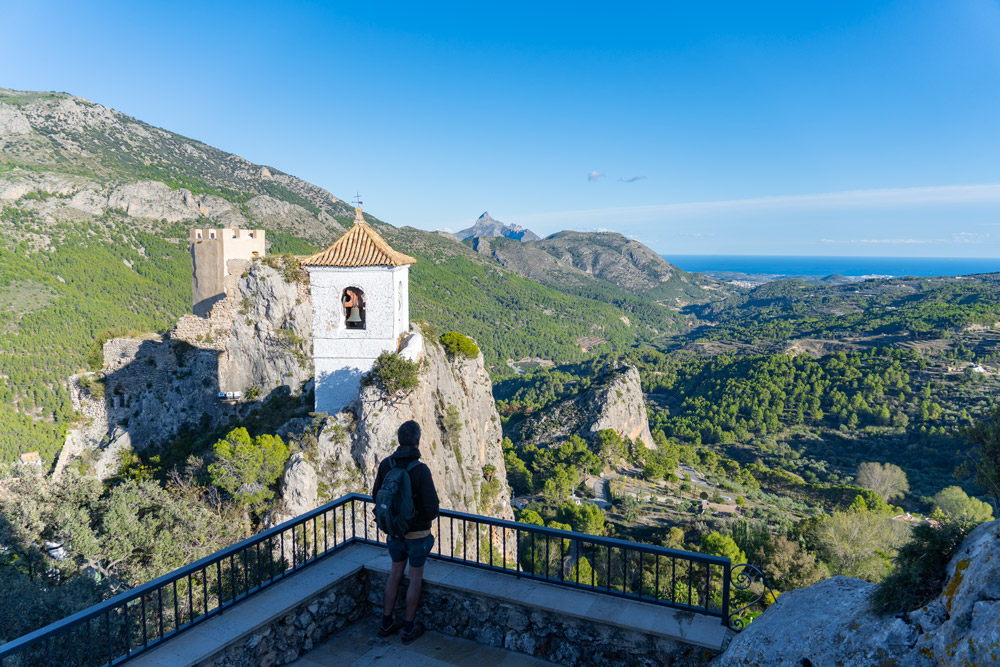 Un chico en un mirador contemplan las vistas desde un pueblo en la Sierra de Alicante. Se ve el valle y el mar al fondo.