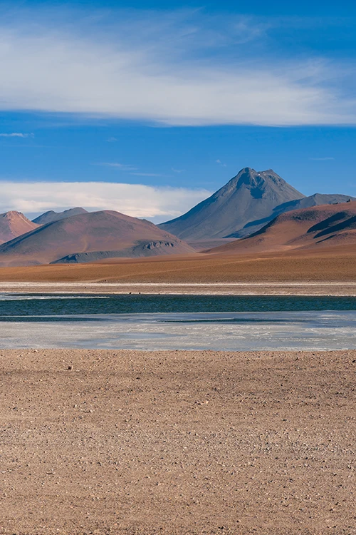 Una laguna de un salar se ve con un volcán al fondo. Foto vertical. Otro magnífico lugar que ver en el desierto de Atacama.