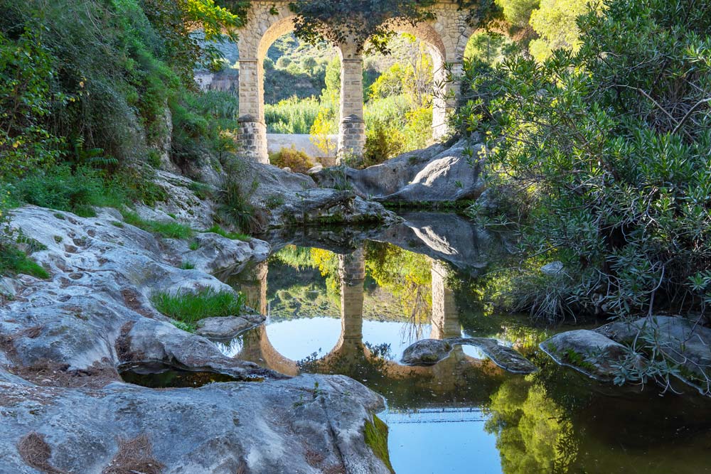 Reflejo de un puente romano sobre las charcas de agua.