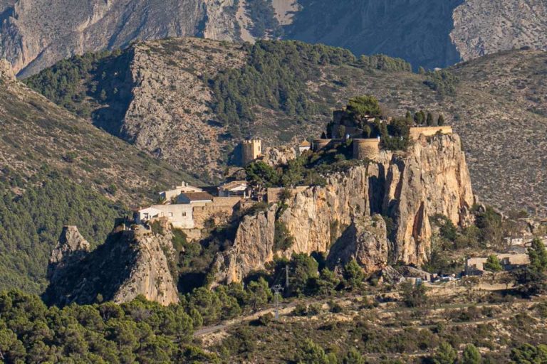 Vista a lo lejos de un castillo que se encuentra ubicado encima de un peñón de piedra. Qué ver en Guadalest. Un pueblo mágico que no te debes perder. Perder el Rumbo.