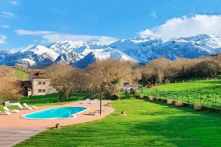 Una de las Casas rurales en España más bonitas con un verde prado y una piscina y con las montañas nevadas al fondo. Un paisaje espectacular en un día soleado