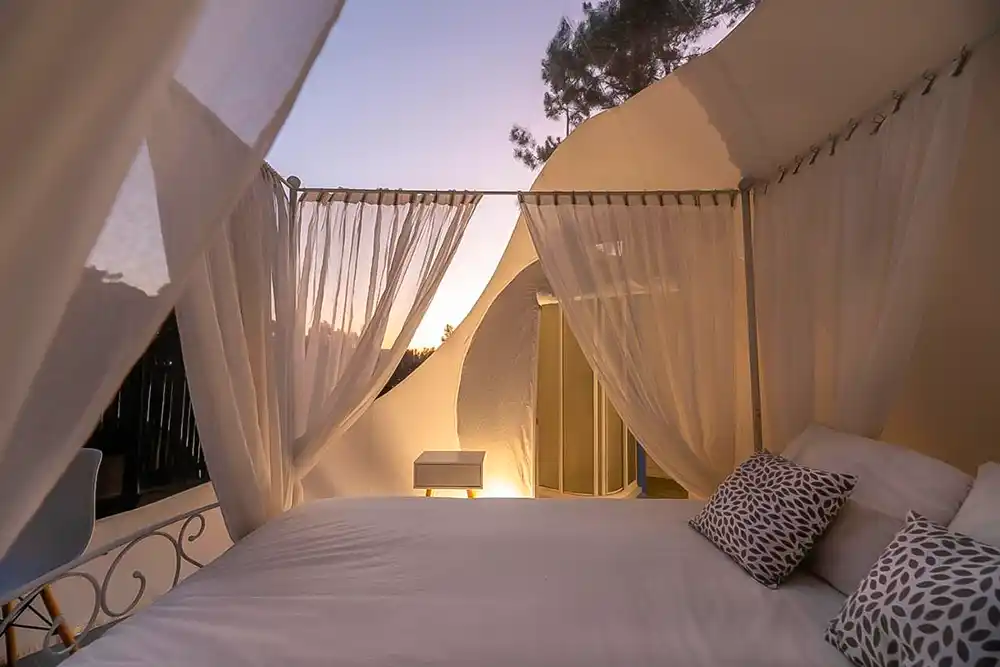 Interior de un hotel burbuja donde se ve la cama, las cortinas que a rodean y las vistas panorámicas al cielo