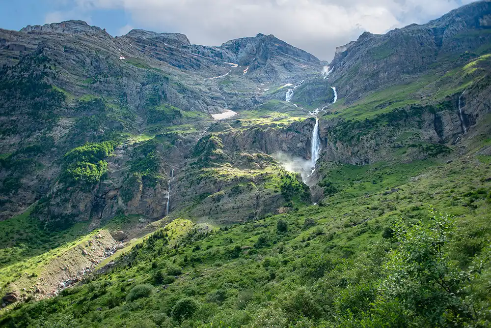 Podemos ver la cascada de Cinca rodeada de montañas y vegetación.
