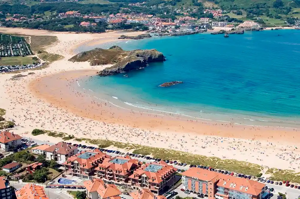 Vista aérea de una playa rodeada de edificios. La playa está abarrotada de gente.