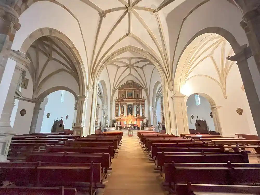 Interior de la iglesia con su retablo pintado al fondo y bóvedas de crucería.