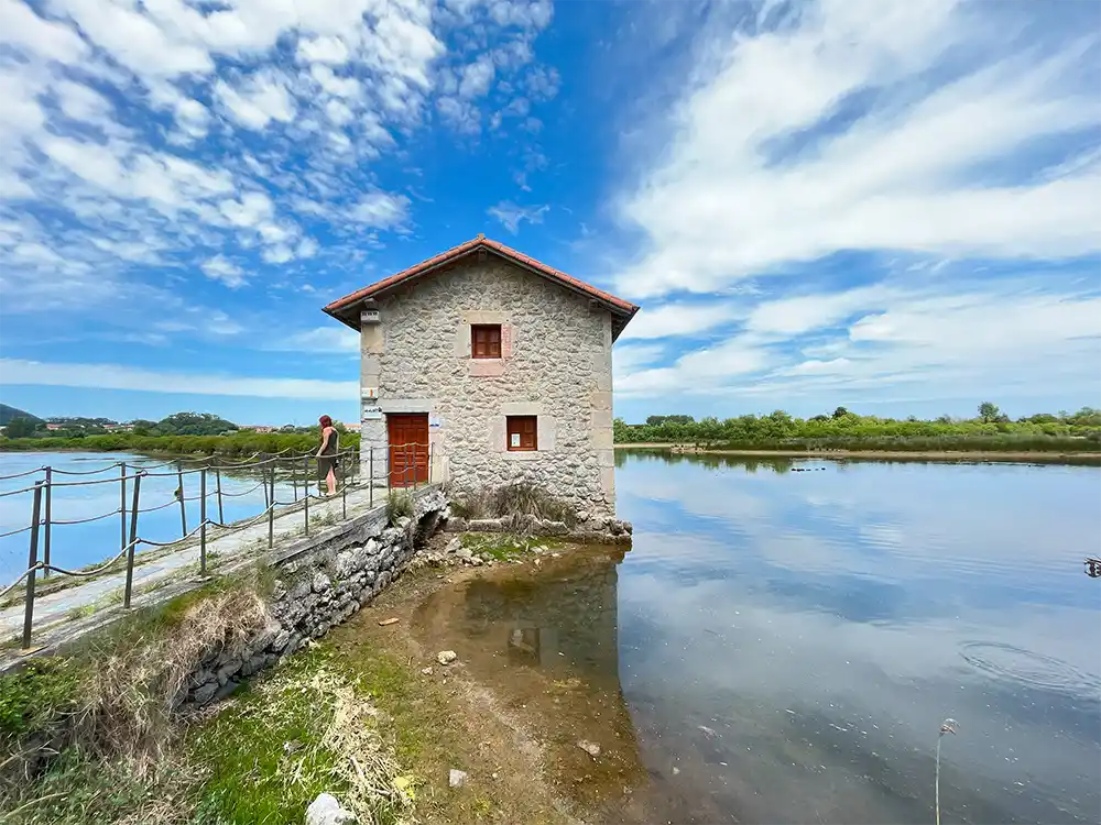 Un Molino de mareas y una chica en una pasarela que divide las dos zonas de agua. La construcción es de piedra.