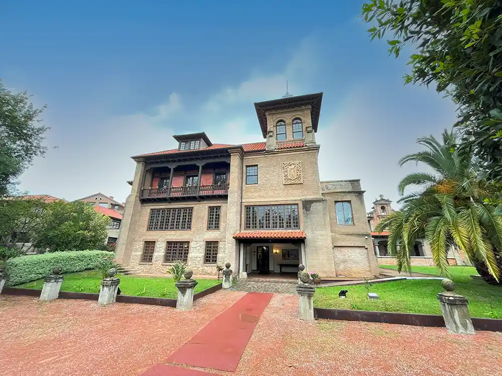 Una casa señorial con un balcón y una torre. La casa tiene unos grandes jardines.