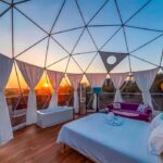 Interior de un domo, muestra de las maravillas que nos ofrecen los hoteles burbuja en Portugal. Se ve el cielo azulado en una puesta de sol y la habitación con bañera de hidromasaje.