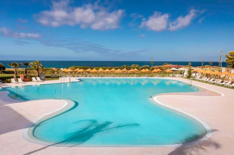 Gran piscina de color turquesa con sombrillas y vistas al mar. Sin duda, es uno de los mejores hoteles en Conil con mucho encanto.