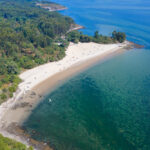 Vista aérea de una de las preciosas playas de Rianxo de arena blanca rodeada de árboles y con aguas transparentes.