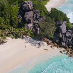 Plano aéreo de una playa de La Digue con arena blanca, aguas turquesas y rocas graníticas de formas impresionantes. Es una auténtica belleza, un paraíso. Esta foto es la portada del artículo Qué ver y qué hacer en La Digue, de Perder el Rumbo.
