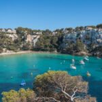Vista de Cala Galdana con su preciosa playa de aguas turquesas y sus acantilados con casitas en la cima. Sin duda, una de las mejores zonas donde alojarse en Menorca