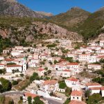 Vista desde lo alto de Dhermi, un precioso pueblo costero de Albania, con sus casas blancas y de piedra y su iglesia con el campanario azul. Al fondo se ven grandes montañas.