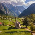 Vista panorámica del valle de Theth en los Alpes Albaneses, destacando la icónica iglesia de piedra en medio de prados verdes.
