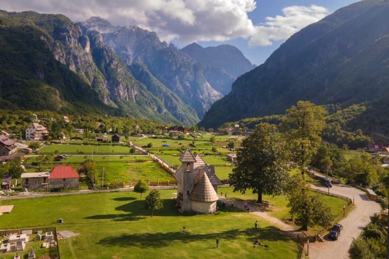 Vista panorámica del valle de Theth en los Alpes Albaneses, destacando la icónica iglesia de piedra en medio de prados verdes.